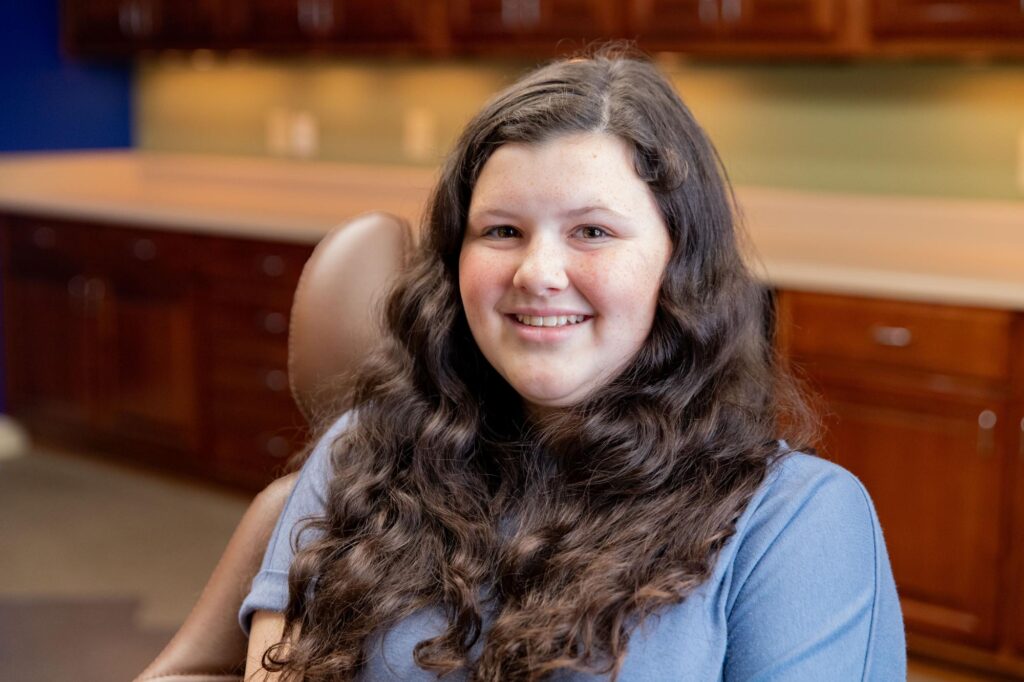 Smiling teen patient with long brown hair seated in a treatment chair at Ryan Cox Orthodontics in Rome, GA